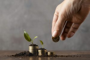 front-view-hand-adding-coins-stack-covered-dirt-plants